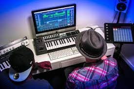 Two musicians collaborate at a computer workstation with music production software and instruments.